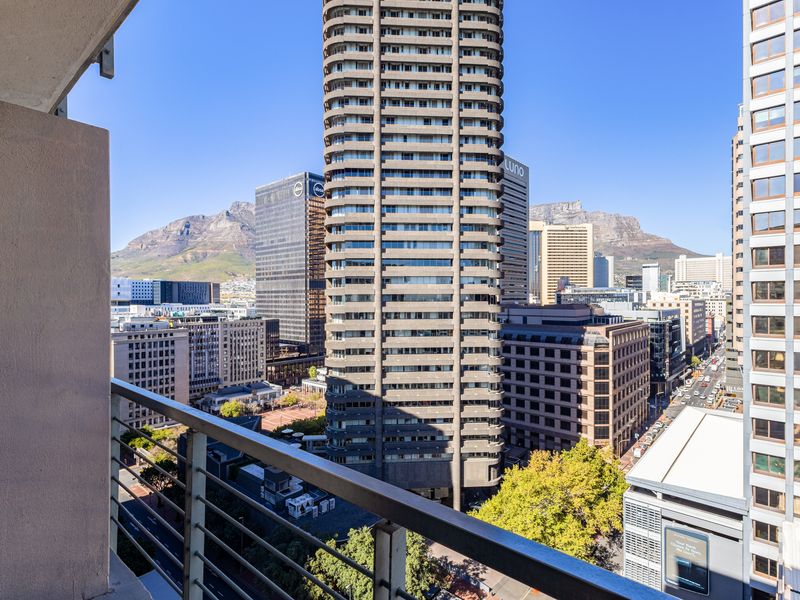 Elevated city view from a balcony overlooking surrounding high-rise buildings and mountain scenery.