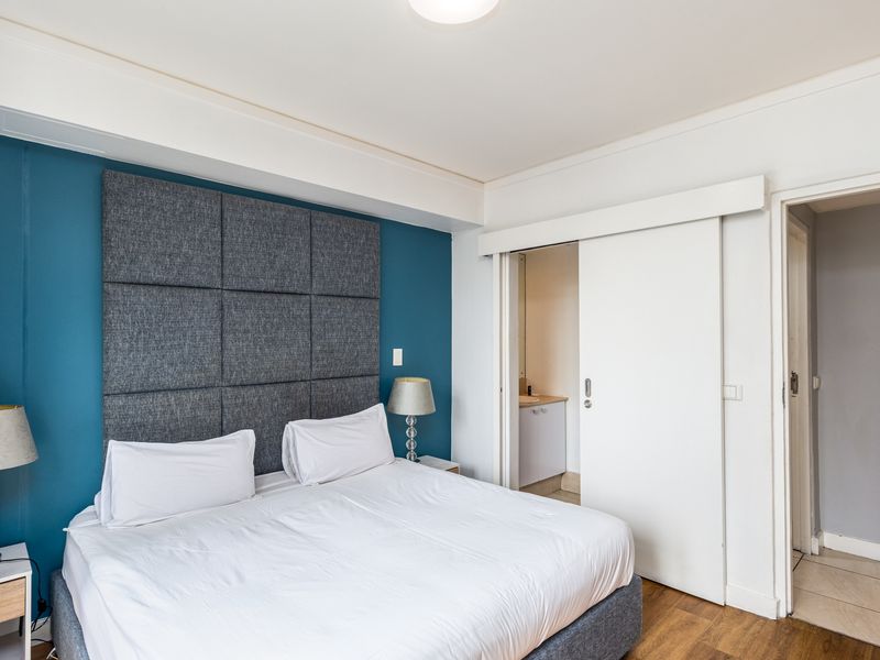 A well-maintained bedroom featuring laminate flooring, a feature wall with integrated headboard, and direct access to an en-suite bathroom via a sliding door.