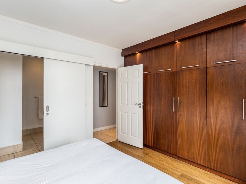 A well-maintained bedroom featuring extensive built-in wooden cabinetry with integrated lighting, laminate flooring, and direct access to an en-suite bathroom.