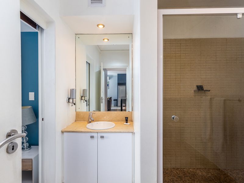 A functional bathroom featuring a vanity with stone countertop, integrated basin, and a glass-enclosed shower with mosaic tiling.
