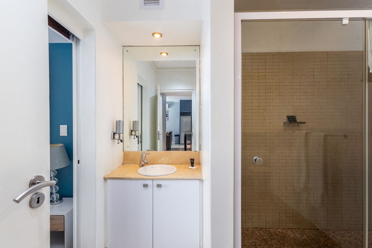 A functional bathroom featuring a vanity with stone countertop, integrated basin, and a glass-enclosed shower with mosaic tiling.