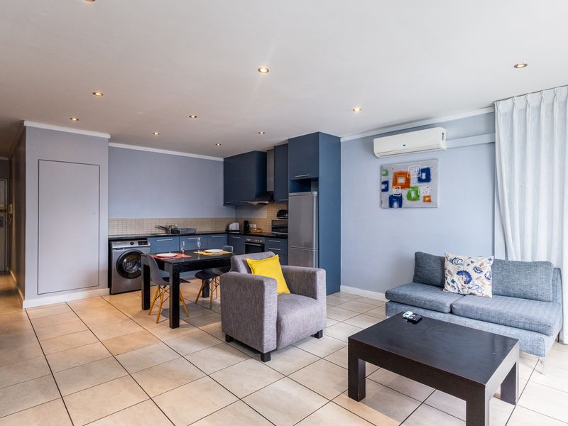 Open-plan living area featuring a modern kitchen with built-in cabinetry, tiled flooring, and a wall-mounted air conditioning unit.