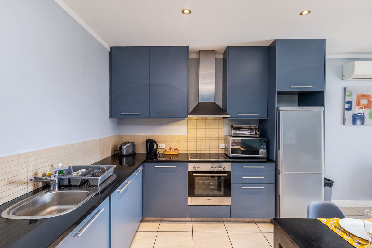 Modern kitchen featuring blue cabinetry, black granite countertops, stainless steel appliances, tiled backsplash, and integrated lighting.