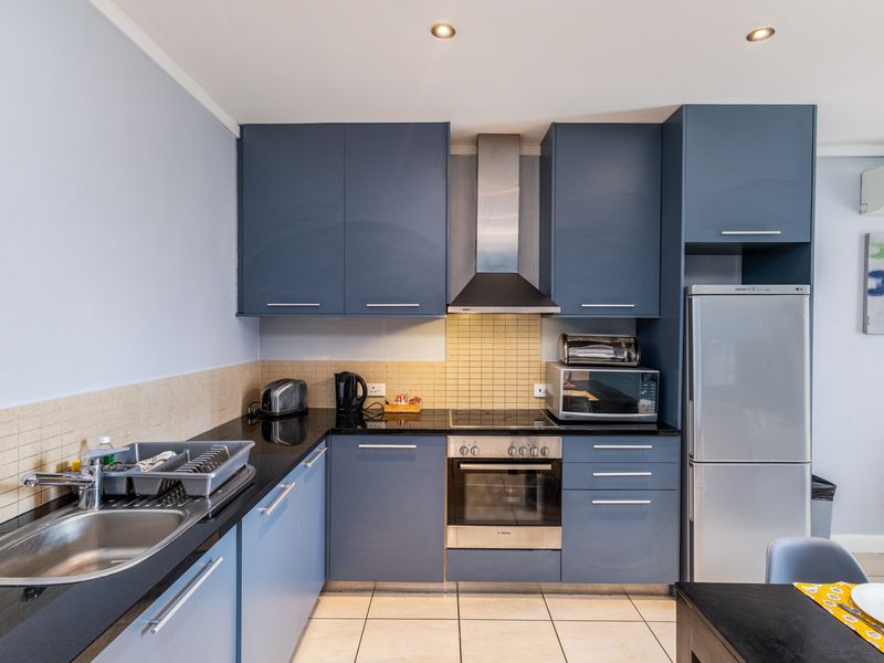 Modern kitchen featuring blue cabinetry, black granite countertops, stainless steel appliances, tiled backsplash, and integrated lighting.