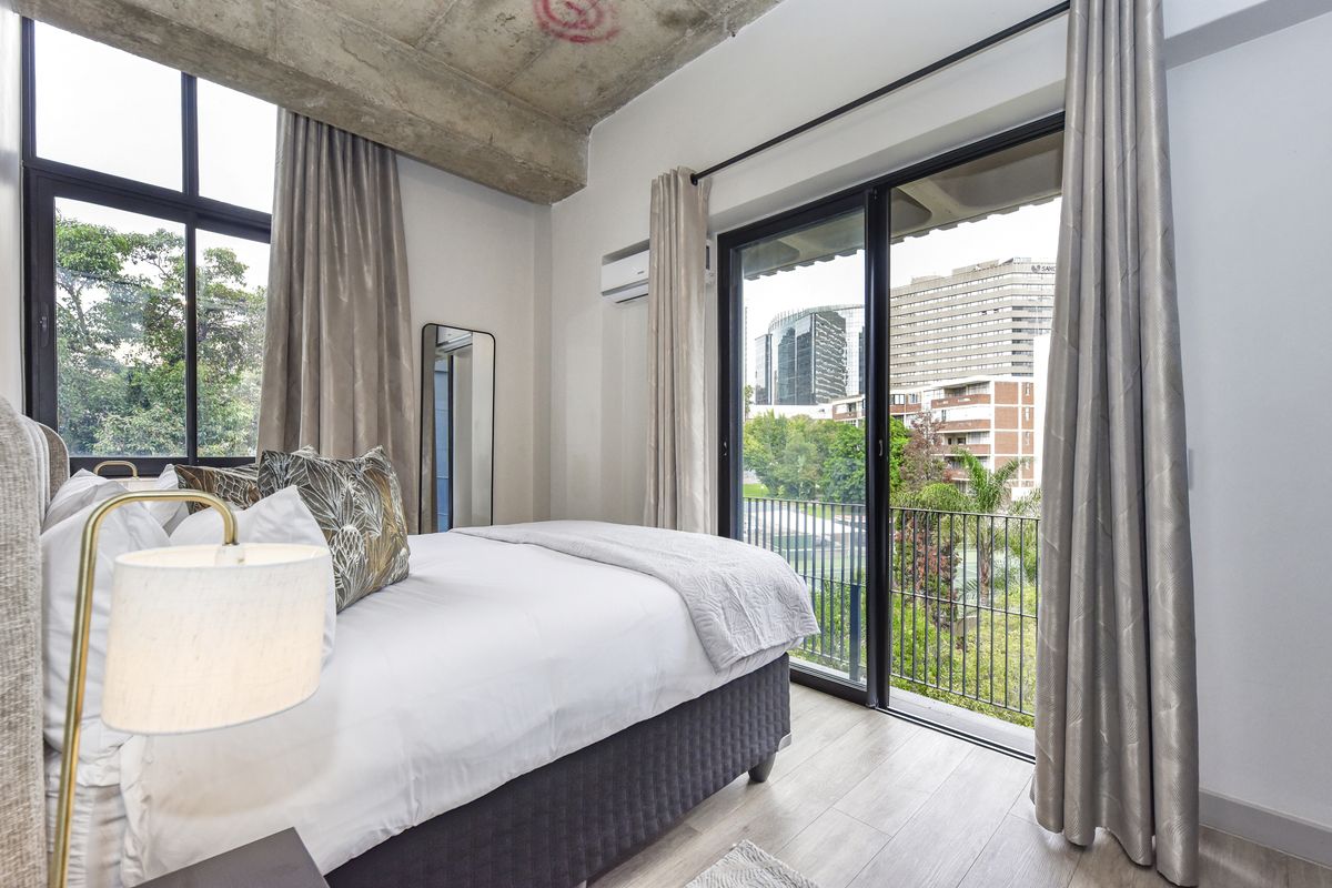 Modern bedroom featuring an exposed concrete ceiling, laminate flooring, and large sliding glass doors opening to a balcony with urban views.