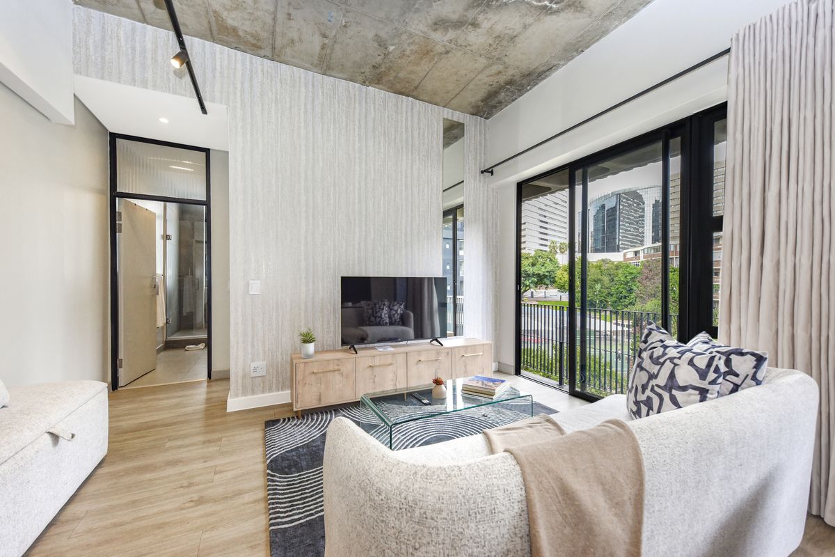 Modern living room featuring an exposed concrete ceiling, textured feature wall, and large sliding glass doors leading to a balcony with urban views.