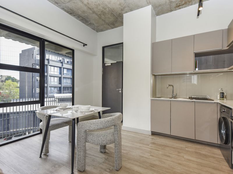 Modern open-plan apartment featuring a sleek kitchen with built-in appliances, exposed concrete ceiling, and large glass doors leading to a balcony.