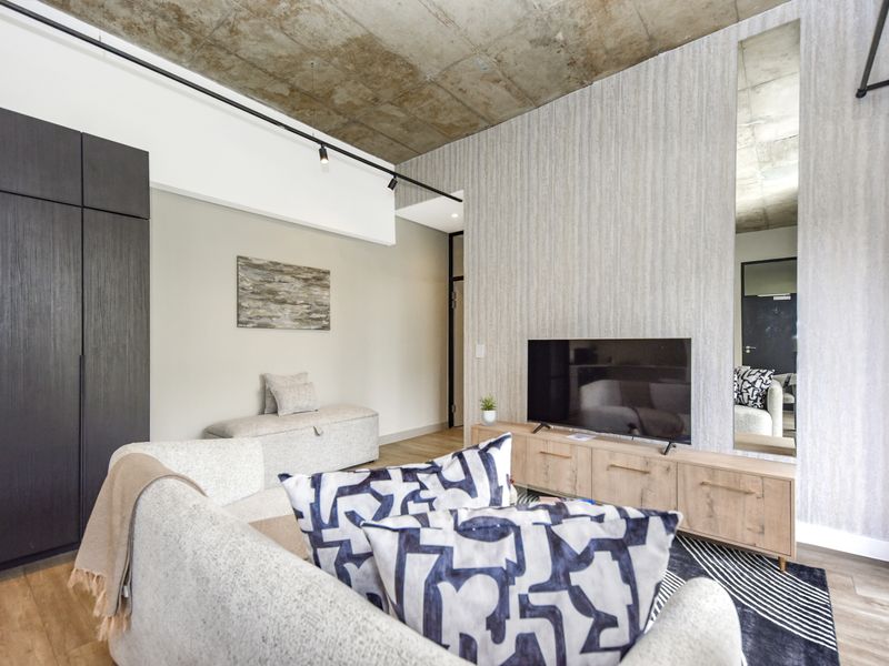 Modern living room featuring an exposed concrete ceiling, track lighting, and sleek built-in cabinetry with a full-length wall mirror.