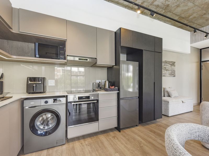 Modern kitchen featuring sleek cabinetry, integrated appliances, glass splashback, and an industrial-style exposed concrete ceiling with track lighting.