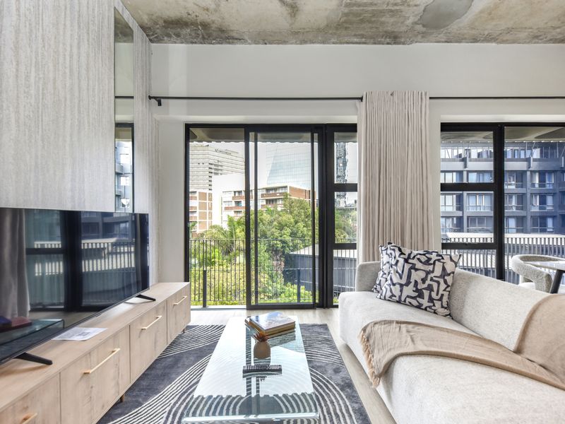 Modern living room featuring an exposed concrete ceiling, textured feature wall, and large sliding glass doors opening to an urban balcony view.