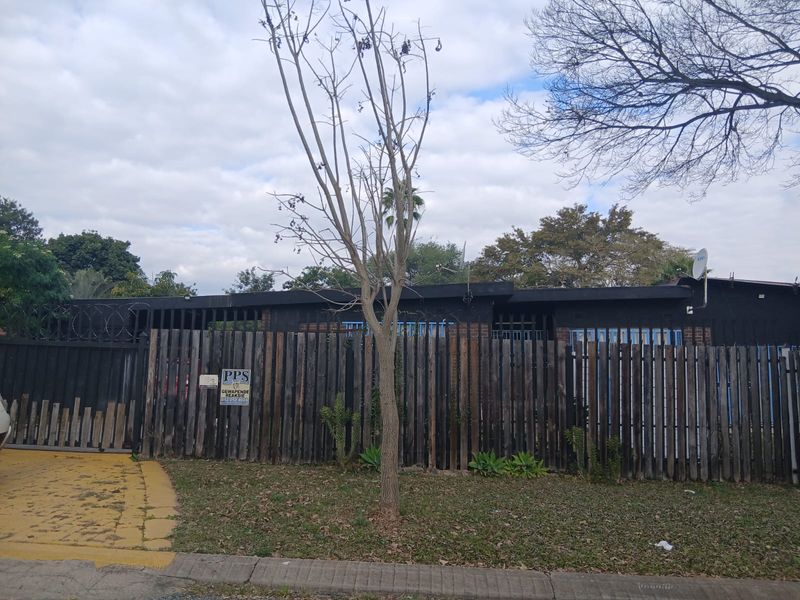Front exterior view of a residential property featuring a timber fence, security razor wire, and a paved driveway.