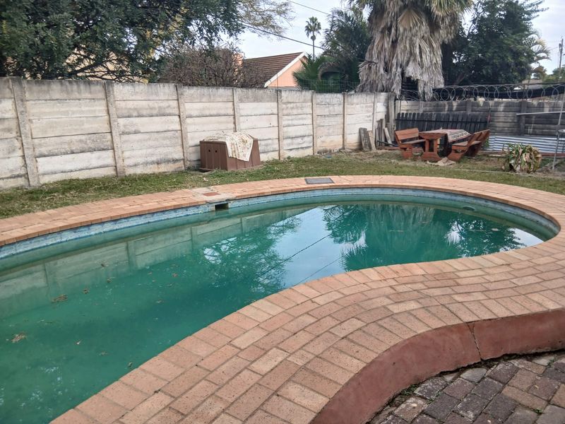 Outdoor pool area featuring a curved brick-edged swimming pool, enclosed by a precast concrete boundary wall with security razor wire.