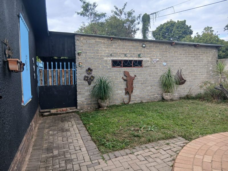 A rear exterior view featuring a brick boundary wall, paved walkway, and secure gated access to the property.