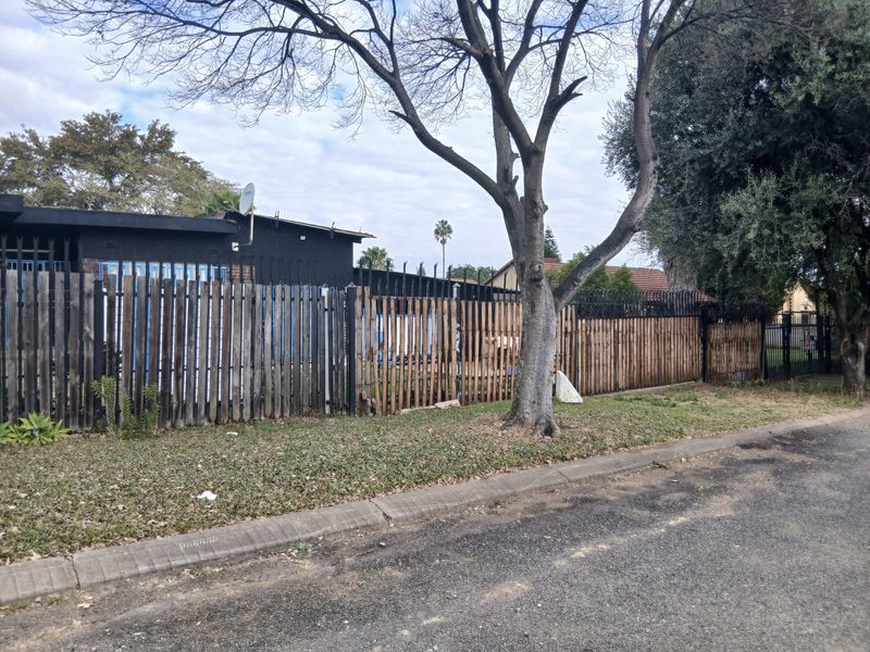 Street view of the property frontage featuring weathered wooden perimeter fencing with integrated metal security spikes and a concrete curb.