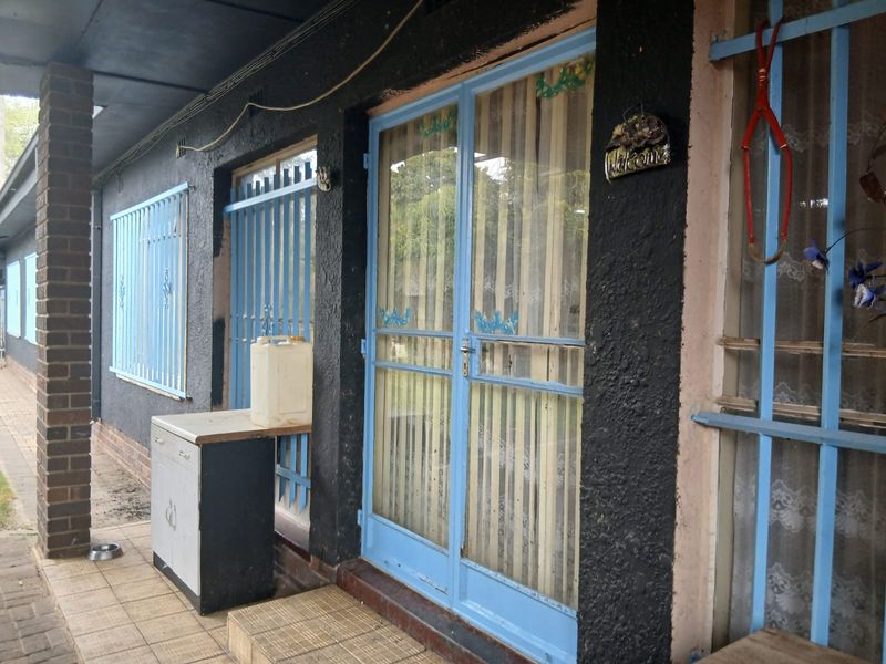 Covered patio area featuring tiled flooring, security bars on windows and doors, and a brick support pillar.
