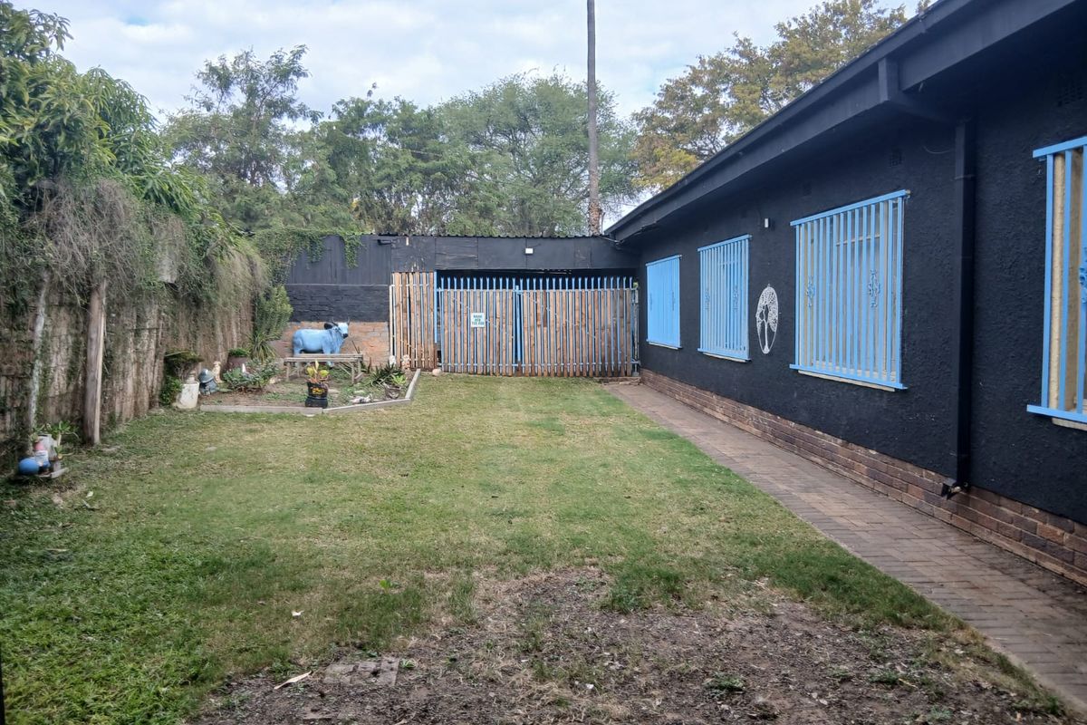 A rear garden area featuring a paved walkway, lawn, and a dark-painted exterior wall with blue security bars on the windows.