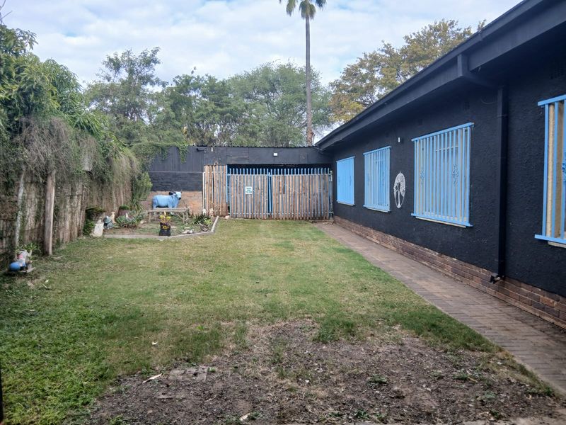 A rear garden area featuring a paved walkway, lawn, and a dark-painted exterior wall with blue security bars on the windows.