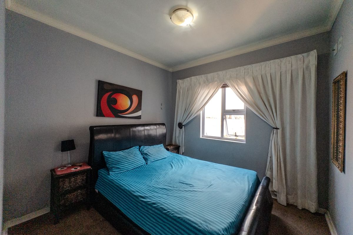 A standard bedroom featuring neutral wall paint, ceiling cornicing, and an aluminium-framed window with curtain tracks.