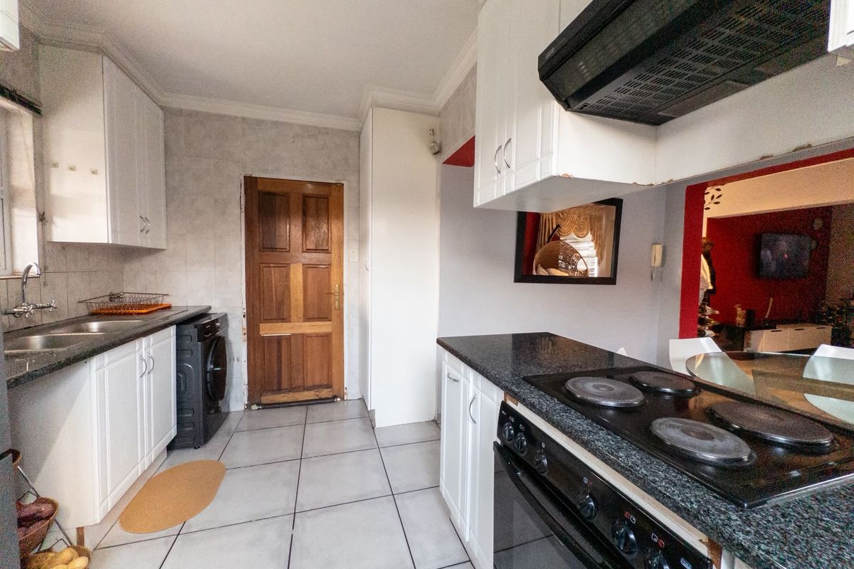 Functional kitchen featuring white cabinetry, granite countertops, built-in oven, electric hob, and tiled flooring with direct access to the living area.