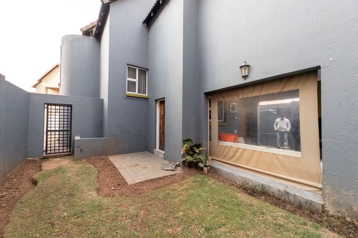 Rear exterior view of the townhouse featuring a paved patio area, small garden space, and a retractable outdoor blind for the patio.