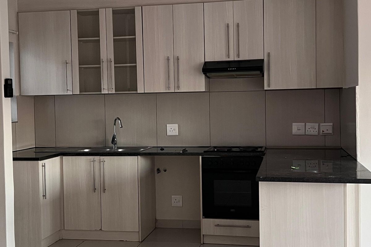 A clean, modern kitchen featuring light wood-finish cabinetry, dark granite countertops, built-in oven, extractor fan, and neutral floor tiles.