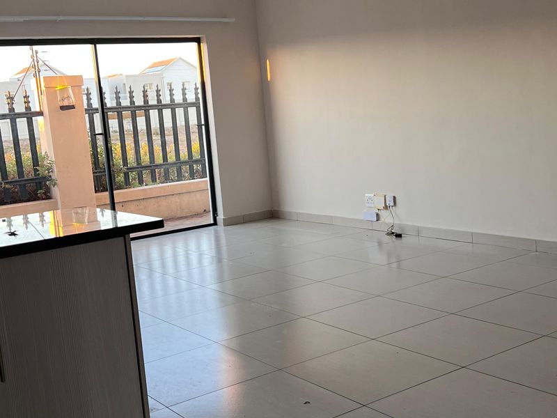 An open-plan living area featuring tiled flooring, a kitchen island, and a sliding glass door leading to an outdoor space.