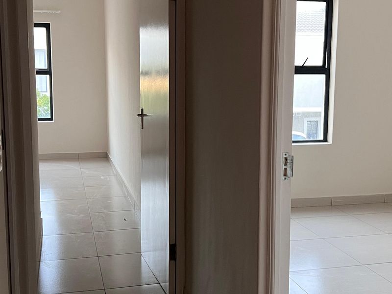 A bright, empty hallway with neutral tiled flooring and clean white walls, providing access to adjacent rooms.