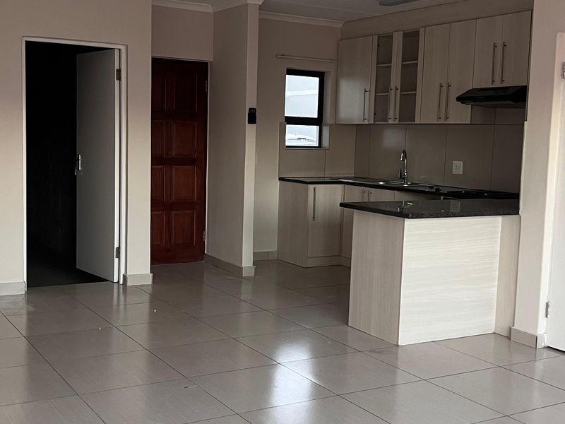 An open-plan living and kitchen area featuring neutral tiled flooring, modern built-in cabinetry with granite countertops, and an integrated extractor fan.