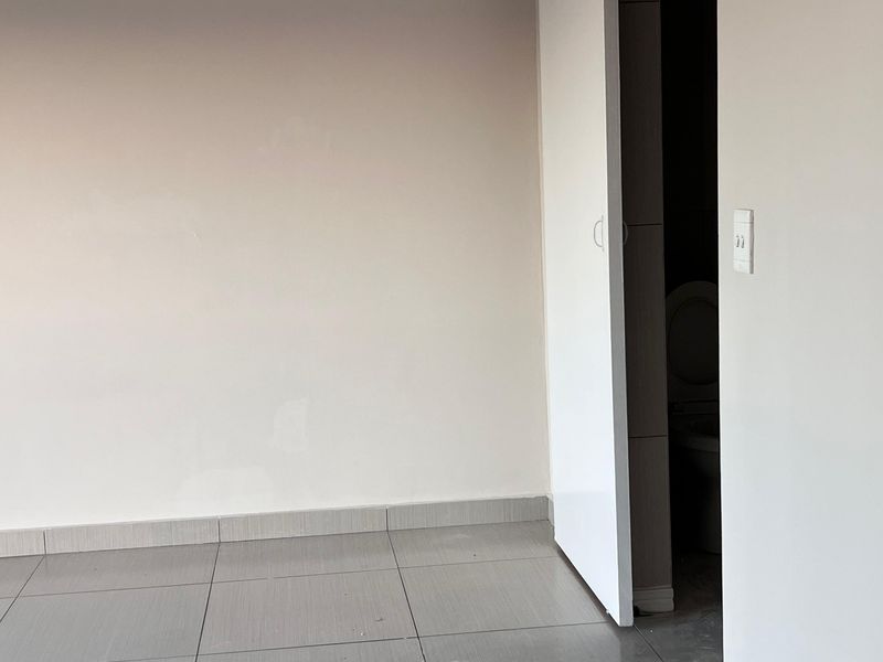 An empty bedroom featuring neutral wall paint, grey ceramic floor tiles, and a modern sliding door leading to an adjacent bathroom.