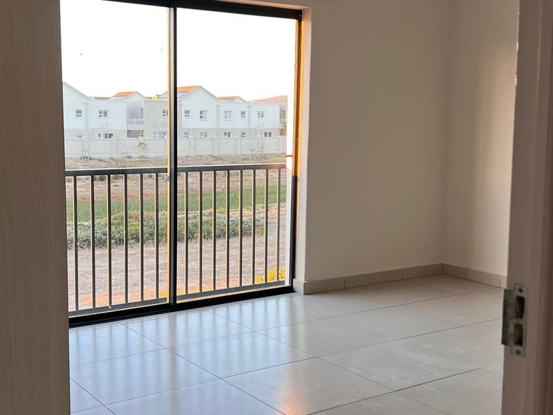 A bright, empty bedroom featuring neutral tiled flooring and a large sliding glass door that provides natural light and access to the exterior.