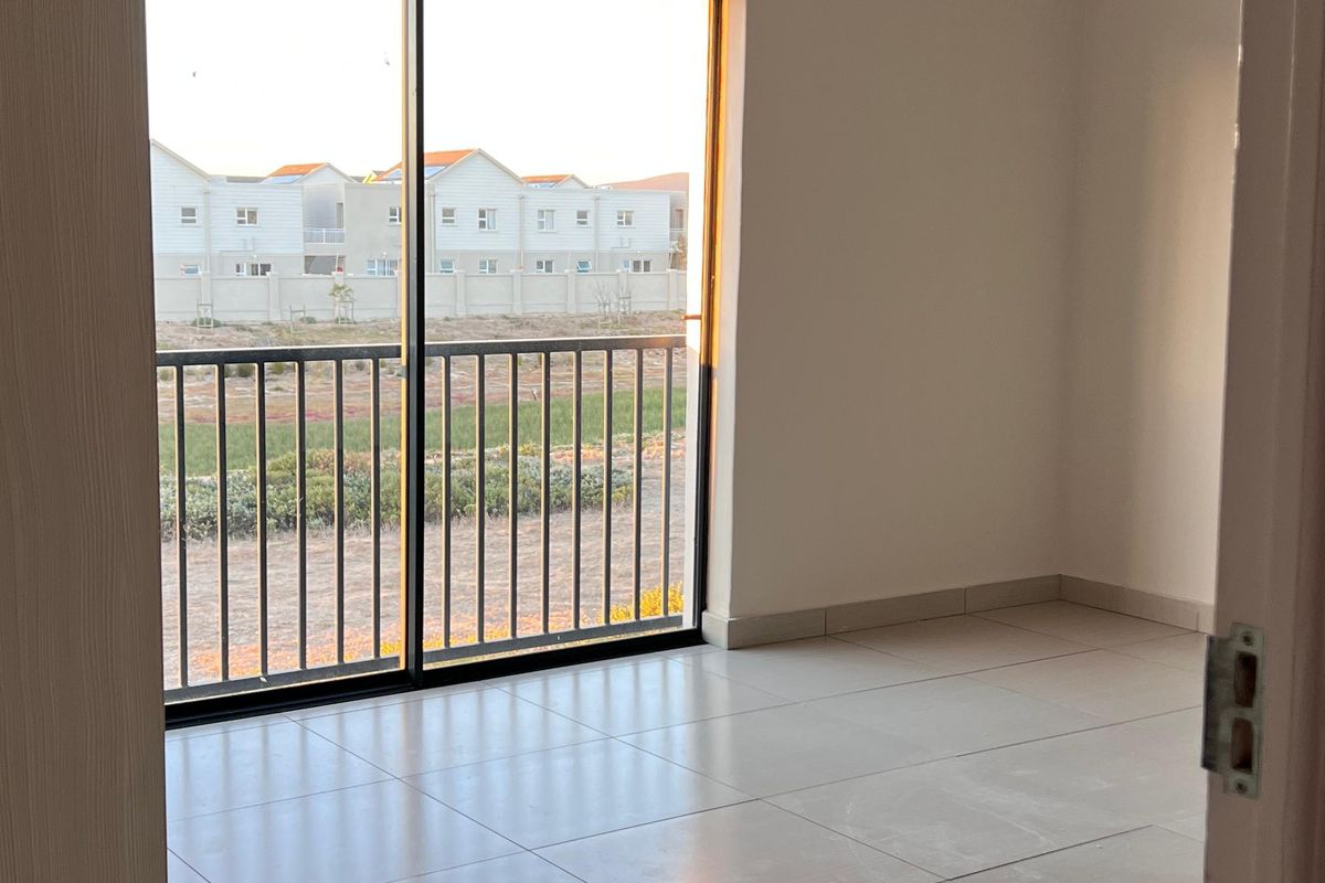 A bright, empty bedroom featuring neutral tiled flooring and a large sliding glass door that provides natural light and access to the exterior.