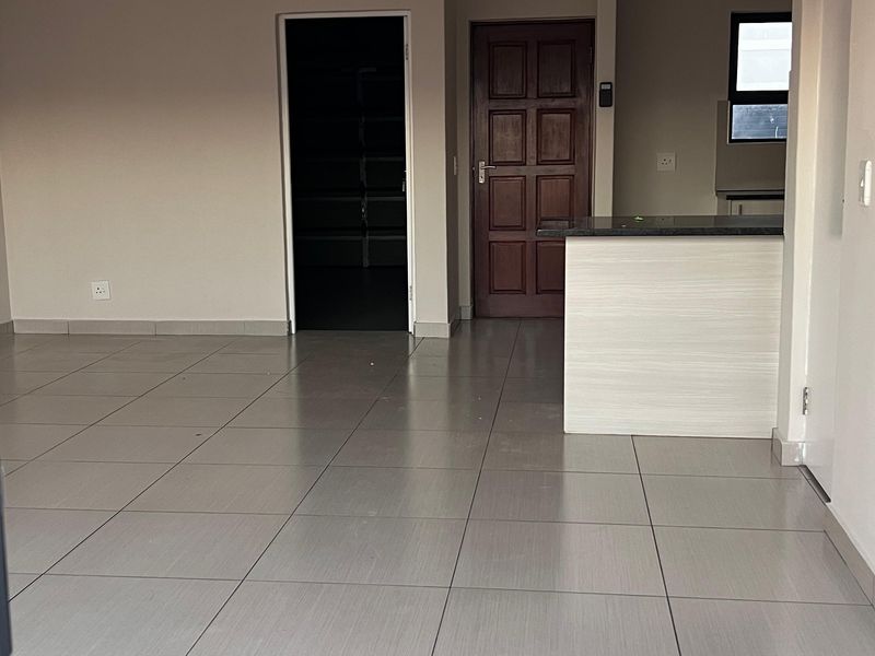 An open-plan living area featuring neutral tiled flooring, a kitchen breakfast bar, and a solid wood entrance door in a well-maintained interior space.