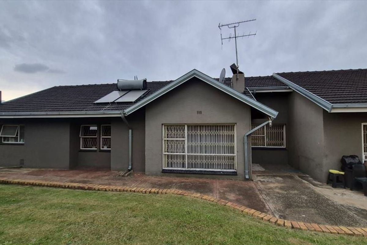 Rear view of the house featuring a tiled roof, solar water heater, security bars on windows, and a paved patio area.