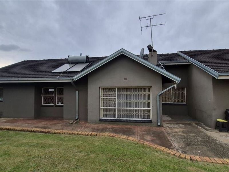 Rear view of the house featuring a tiled roof, solar water heater, security bars on windows, and a paved patio area.