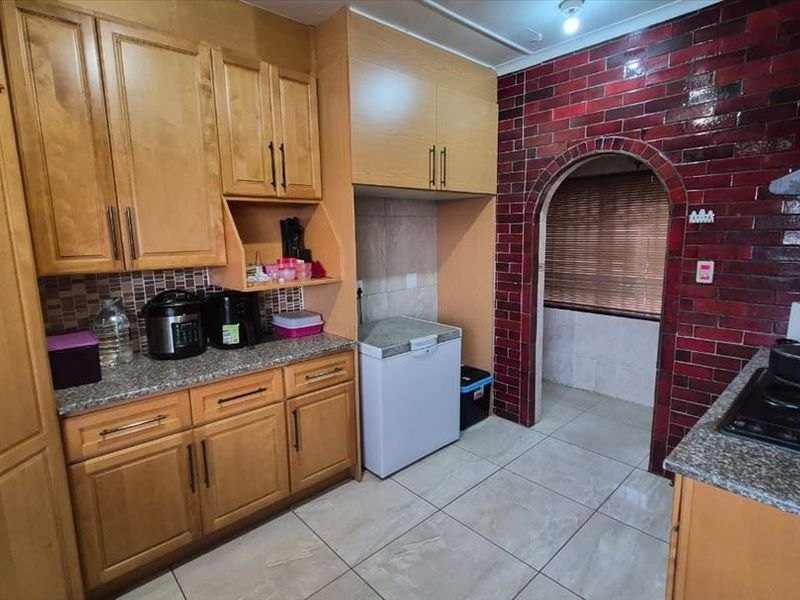 A functional kitchen featuring wooden cabinetry, granite countertops, tiled flooring, and a distinctive red brick feature wall with an arched entryway.