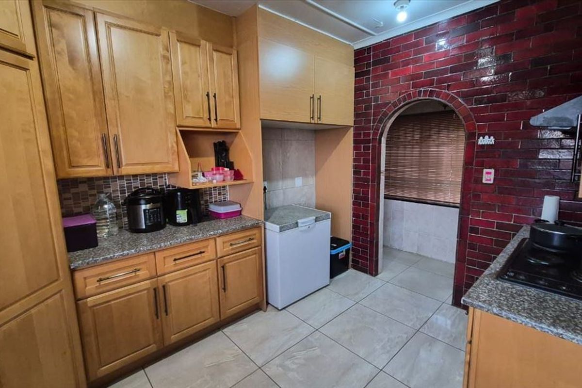 A functional kitchen featuring wooden cabinetry, granite countertops, tiled flooring, and a distinctive red brick feature wall with an arched entryway.
