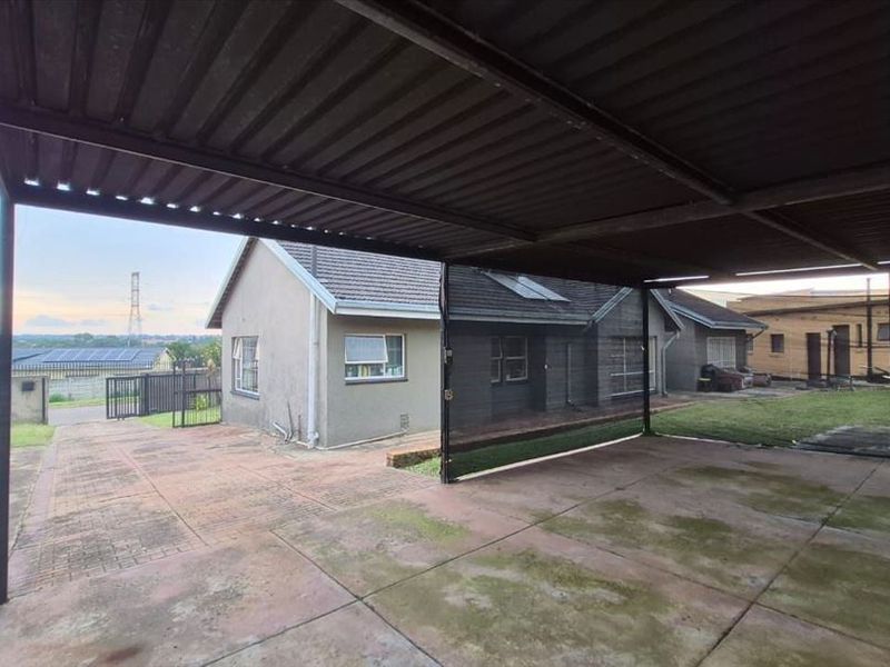 A spacious outdoor carport area with paved flooring, providing covered parking space adjacent to the main residential building.