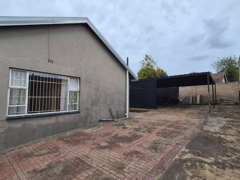 Rear exterior view featuring a paved driveway, a covered carport, and secure boundary walls.