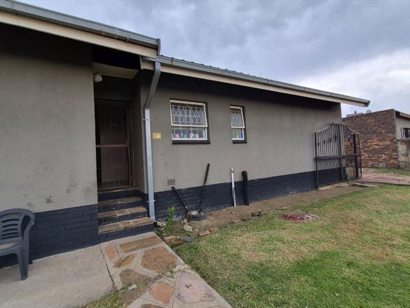 Rear exterior view of the house featuring a paved walkway, security bars on windows, and a small lawn area.