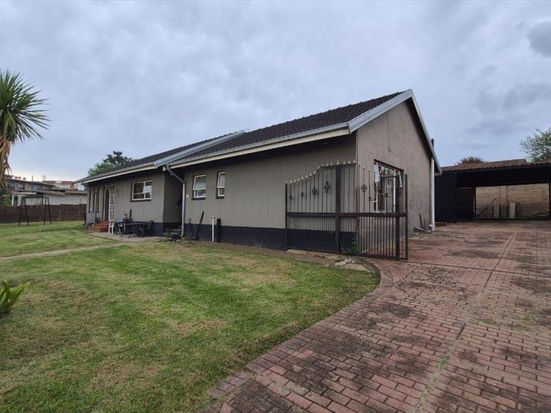 Front view of a single-story house featuring a paved driveway, carport, and a large front lawn with established garden elements.