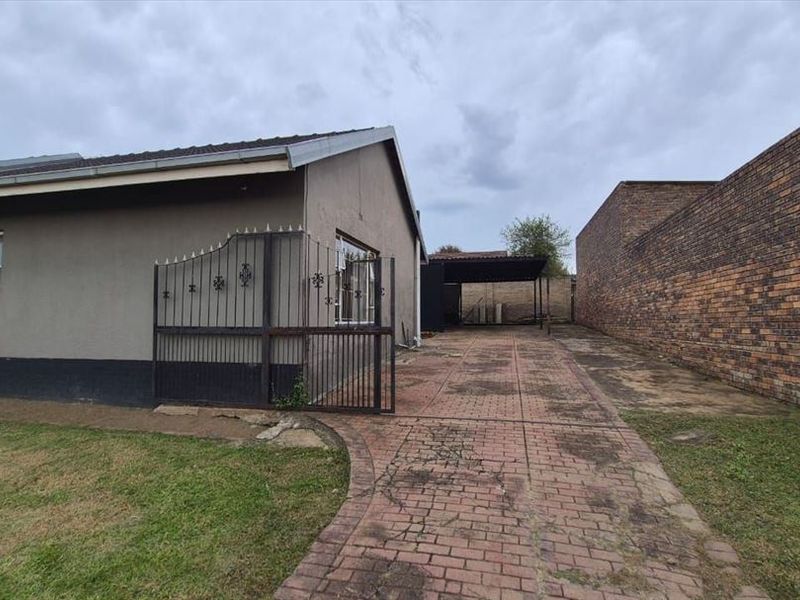 Exterior view of the property featuring a paved driveway, metal security gate, carport, and brick boundary wall.