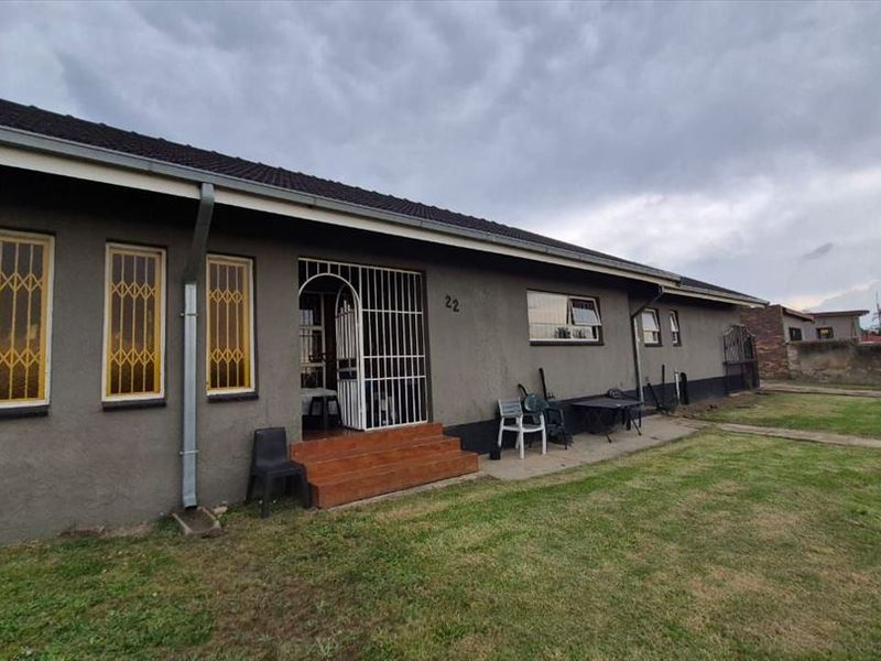 Front elevation of a single-story house featuring security bars on windows, a tiled entrance, and a surrounding lawn area.