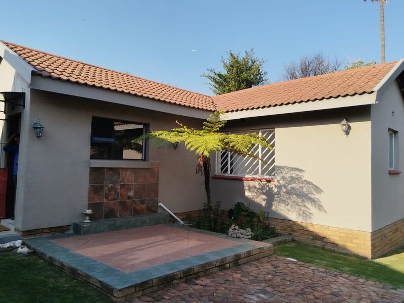Rear view of the cottage featuring a paved patio area, tiled roof, and exterior wall lighting with established garden surroundings.
