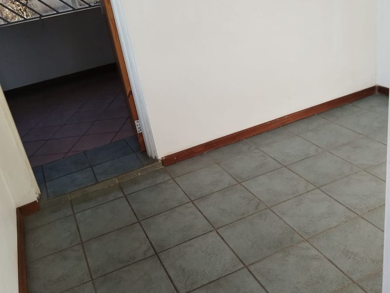 An empty hallway featuring tiled flooring and wooden skirting boards, leading through a doorway to an adjacent tiled area with security bars.