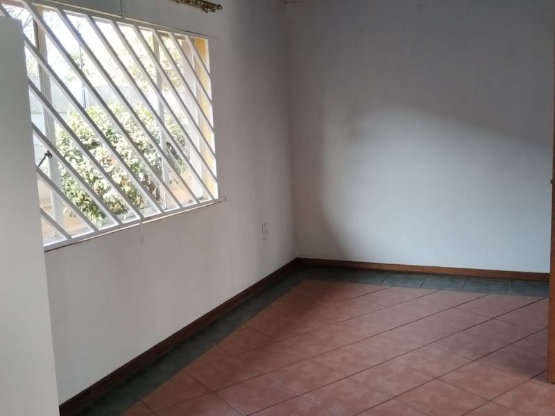 An empty bedroom featuring tiled flooring, security bars on the window, and a painted ceiling, ready for renovation or staging.