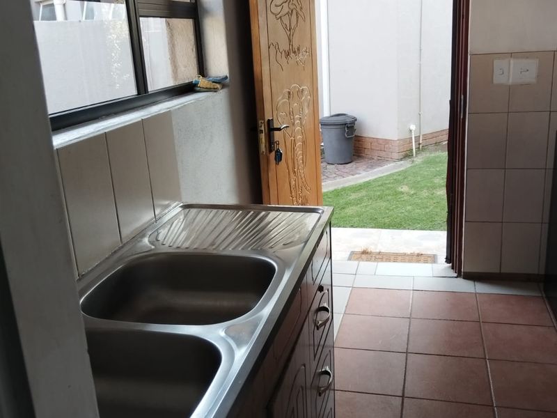 A functional scullery area featuring a double bowl stainless steel sink, tiled splashback, and direct access to the rear garden.