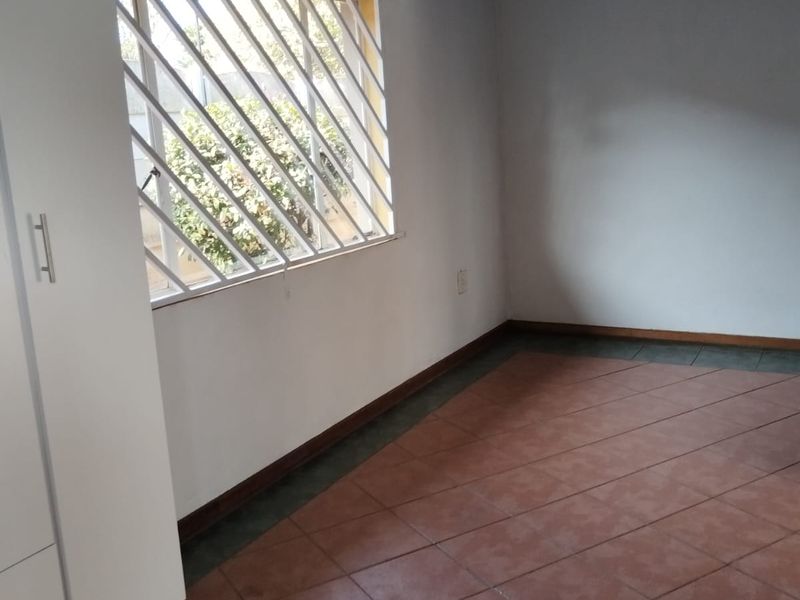 A simple, empty bedroom featuring tiled flooring, a window with security bars, and a blue painted ceiling.
