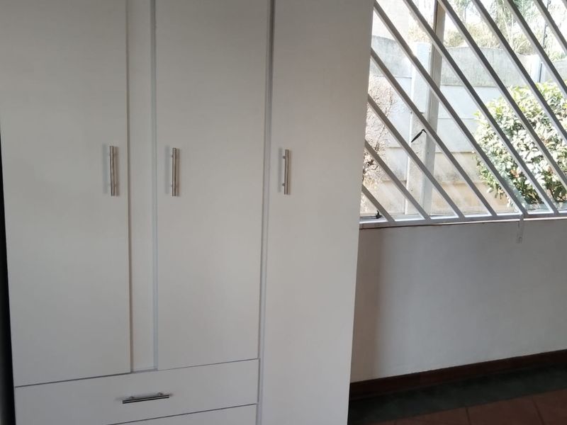 A bedroom featuring tiled flooring, a built-in wardrobe, and a window fitted with security bars.