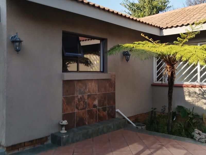 A well-maintained rear exterior view of the cottage featuring a tiled patio area, decorative wall tiling, and secure window fixtures.
