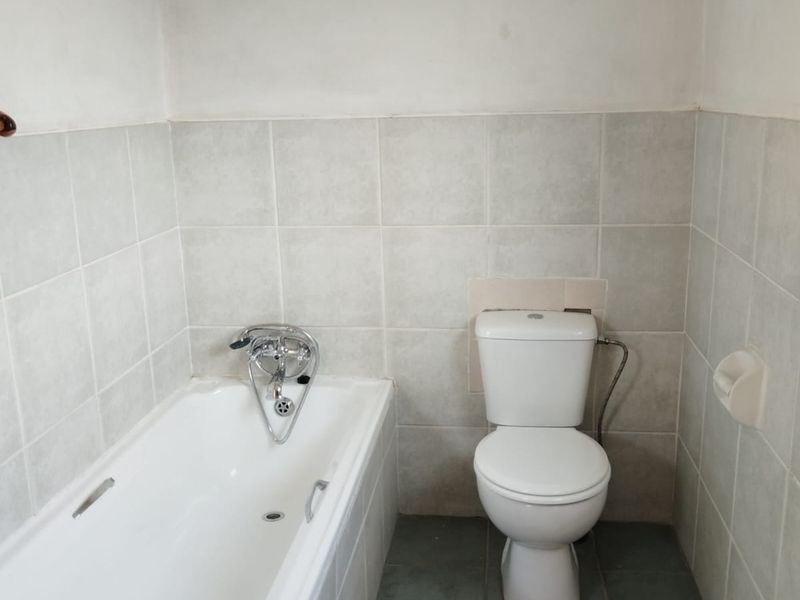 A functional bathroom featuring a standard bathtub, toilet, and neutral wall and floor tiling, currently awaiting final wall finishing.